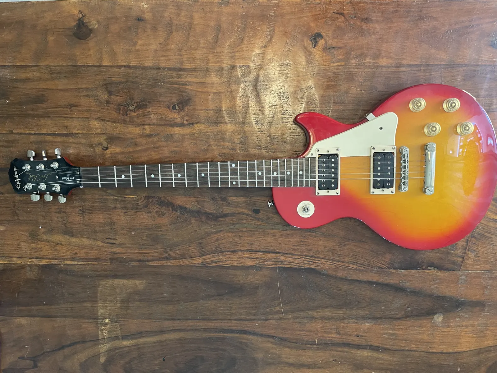 Cherry-sunburst Les Paul-style guitar on a wood bench