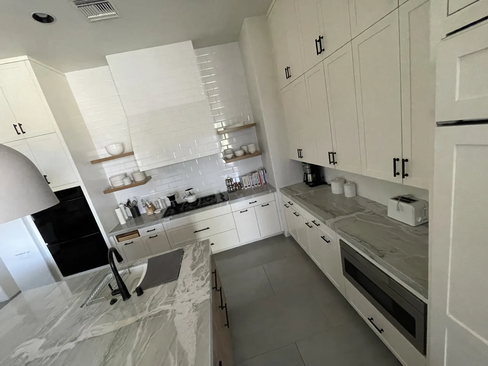 Finished white kitchen with grey marble counters, open shelves and black bar pulls